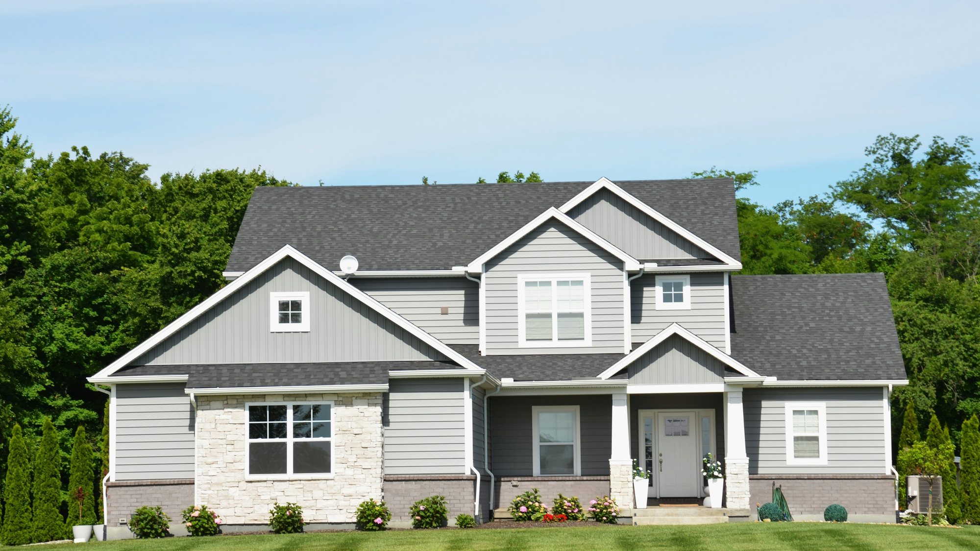 A gray two-story house behind a mown lawn