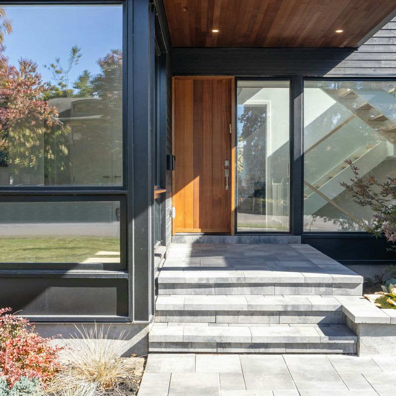 A wood front door set in glass at the entry of a modern house