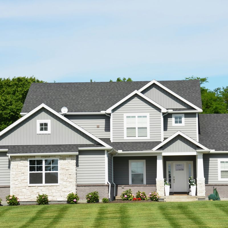 A gray two-story house behind a mown lawn